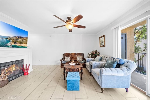 living room with a tiled fireplace, crown molding, and ceiling fan