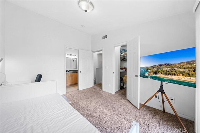 bedroom featuring light colored carpet, a closet, ensuite bath, and a walk in closet