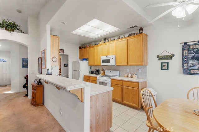 kitchen featuring backsplash, light tile patterned floors, tile counters, kitchen peninsula, and white appliances