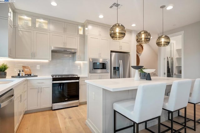 kitchen featuring decorative light fixtures, light hardwood / wood-style flooring, stainless steel appliances, and a kitchen breakfast bar