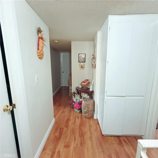 corridor with a textured ceiling and light wood-type flooring