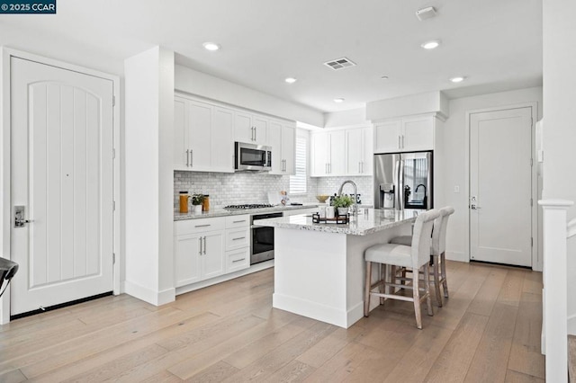 kitchen with white cabinetry, appliances with stainless steel finishes, an island with sink, and light stone counters