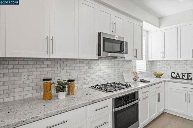 kitchen with stainless steel appliances, white cabinets, light stone counters, and decorative backsplash