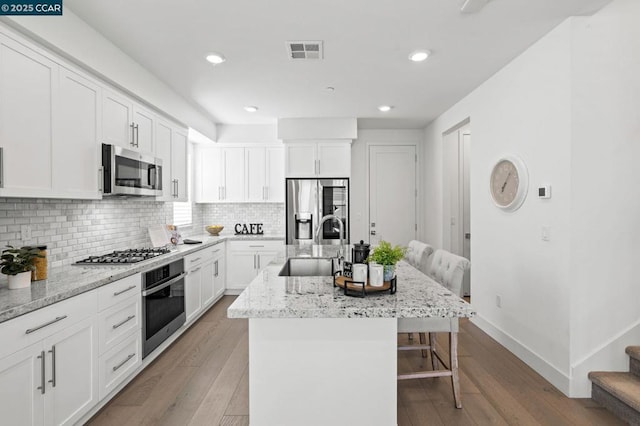 kitchen with a kitchen bar, an island with sink, white cabinets, and appliances with stainless steel finishes