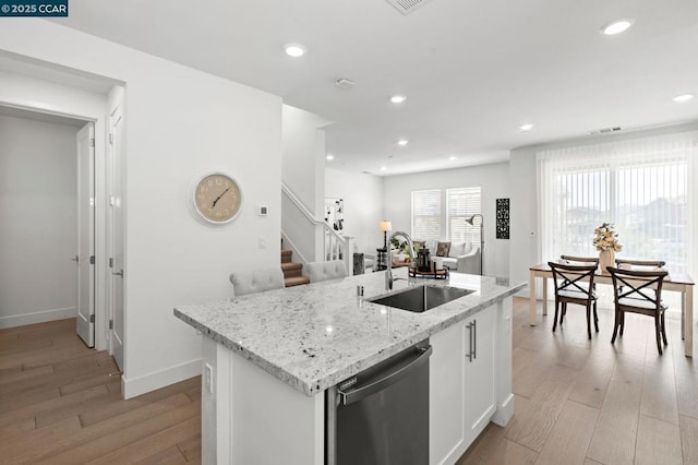 kitchen featuring sink, light hardwood / wood-style flooring, dishwasher, white cabinetry, and a kitchen island with sink