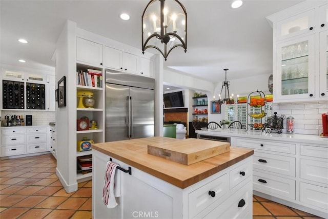 kitchen featuring wooden counters, built in refrigerator, white cabinetry, a center island, and decorative light fixtures