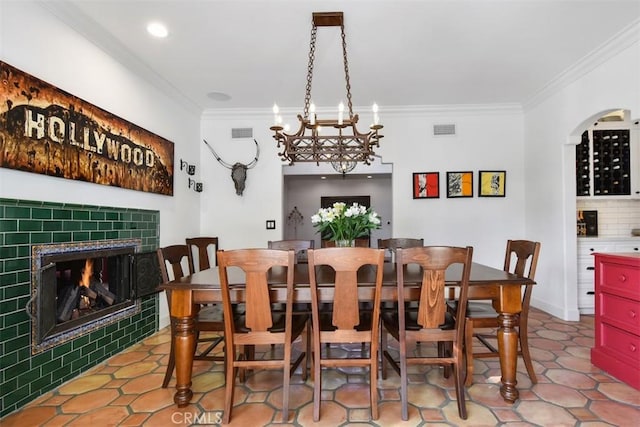 dining space featuring an inviting chandelier, tile patterned flooring, a fireplace, and ornamental molding