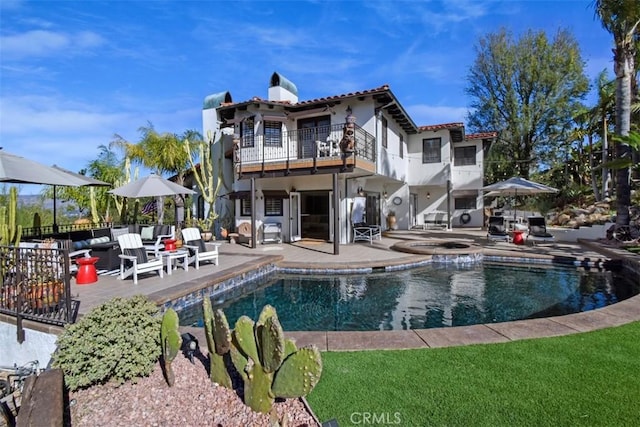 back of property featuring a balcony, a pool with hot tub, and a patio