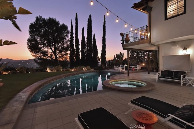 pool at dusk with an in ground hot tub, a mountain view, and a patio area