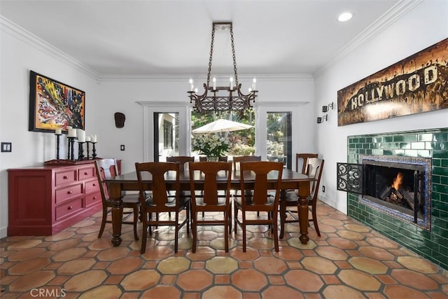 dining space featuring a tiled fireplace, ornamental molding, and an inviting chandelier