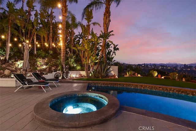 pool at dusk featuring an in ground hot tub