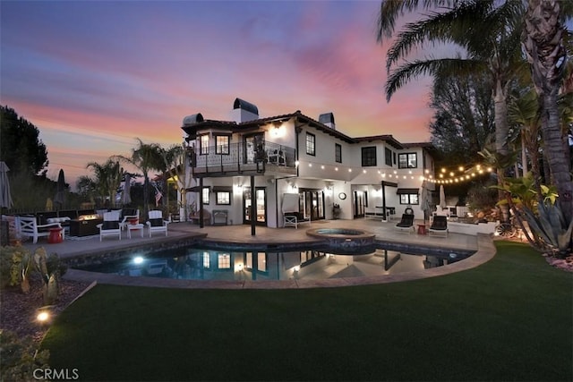 back house at dusk with a balcony, a yard, a patio area, and a pool with hot tub