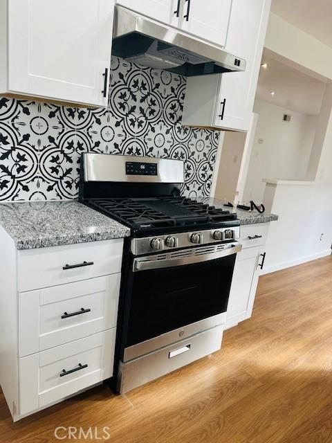 kitchen featuring stainless steel gas stove, white cabinetry, decorative backsplash, light stone countertops, and light hardwood / wood-style flooring