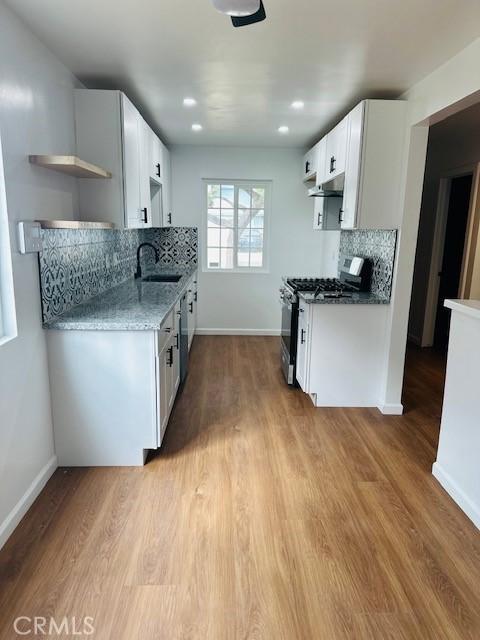 kitchen with white cabinetry, stainless steel gas range oven, sink, and light hardwood / wood-style flooring