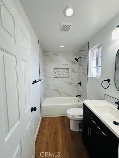 full bathroom featuring hardwood / wood-style flooring, vanity, tiled shower / bath, and toilet