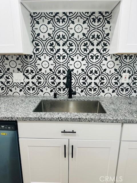 room details with white cabinetry, stainless steel dishwasher, sink, and light stone counters