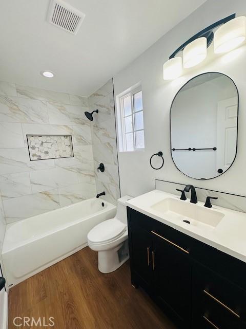 full bathroom with vanity, hardwood / wood-style floors, toilet, and tiled shower / bath