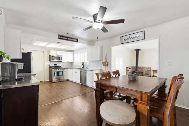 dining room featuring ceiling fan, sink, a wood stove, and dark hardwood / wood-style flooring