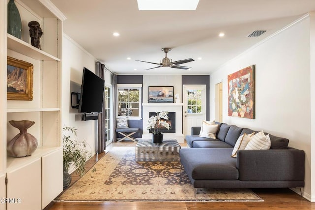 living room featuring ornamental molding, ceiling fan, dark hardwood / wood-style flooring, and a skylight