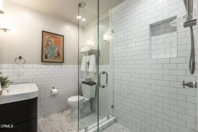 bathroom featuring toilet, a shower with shower door, tile walls, vanity, and tile patterned flooring