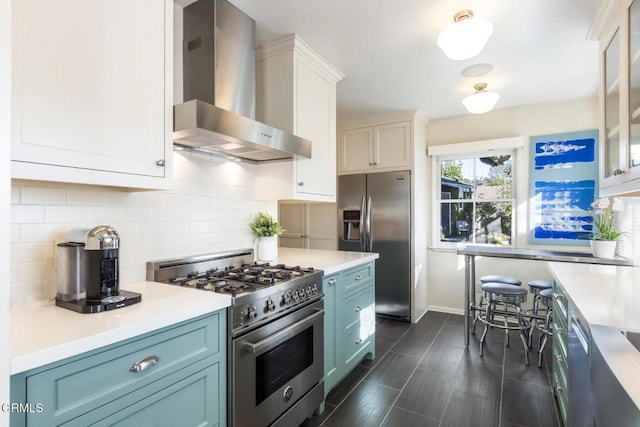 kitchen featuring blue cabinetry, appliances with stainless steel finishes, decorative backsplash, and wall chimney range hood