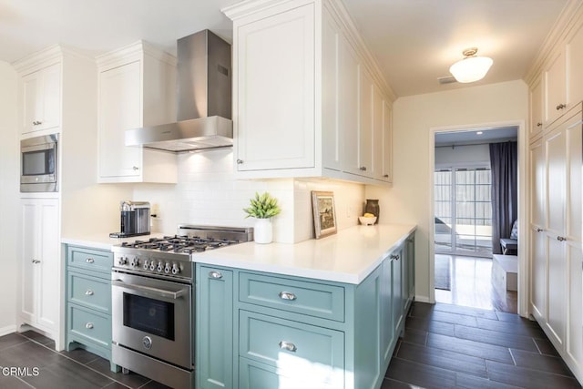 kitchen with dark wood-type flooring, blue cabinets, wall chimney range hood, stainless steel appliances, and white cabinets