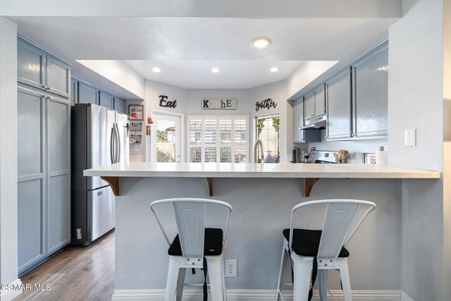 kitchen featuring stainless steel appliances, a breakfast bar, light hardwood / wood-style floors, and kitchen peninsula