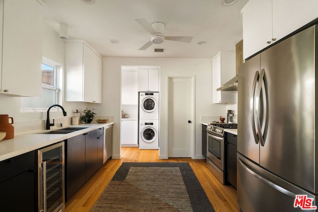 kitchen with sink, appliances with stainless steel finishes, stacked washer / dryer, wine cooler, and white cabinets