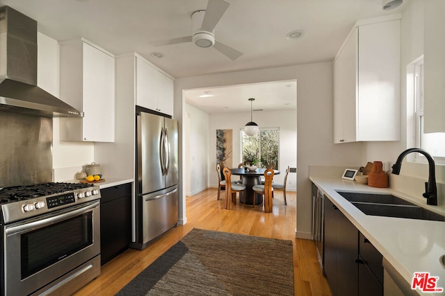 kitchen with pendant lighting, sink, white cabinets, stainless steel appliances, and wall chimney range hood