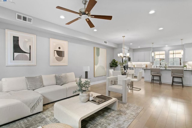 living room with ceiling fan with notable chandelier and light hardwood / wood-style flooring