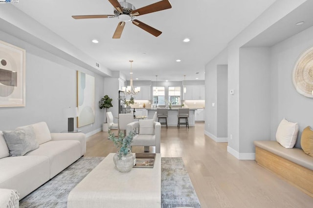 living room with ceiling fan with notable chandelier and light wood-type flooring