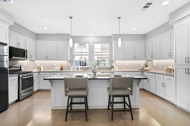 kitchen featuring a kitchen island, appliances with stainless steel finishes, pendant lighting, and white cabinets