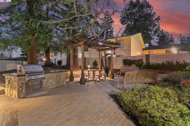 patio terrace at dusk with area for grilling, a grill, and a pergola