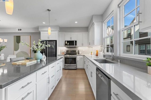 kitchen with sink, white cabinets, dark stone counters, hanging light fixtures, and stainless steel appliances