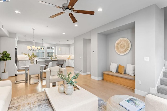 living room featuring ceiling fan with notable chandelier and light wood-type flooring