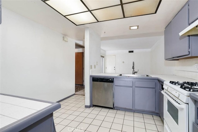 kitchen with sink, white gas range, tile countertops, stainless steel dishwasher, and kitchen peninsula