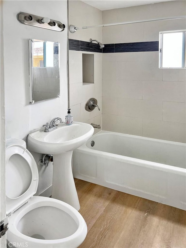 bathroom with hardwood / wood-style flooring, tiled shower / bath, and toilet