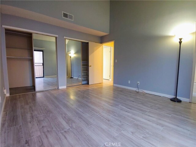 unfurnished bedroom with a towering ceiling, two closets, and light wood-type flooring