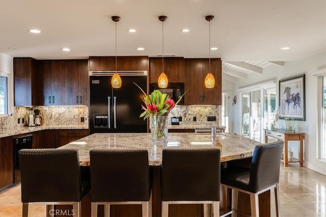 kitchen with light stone countertops, decorative light fixtures, a center island with sink, and black appliances