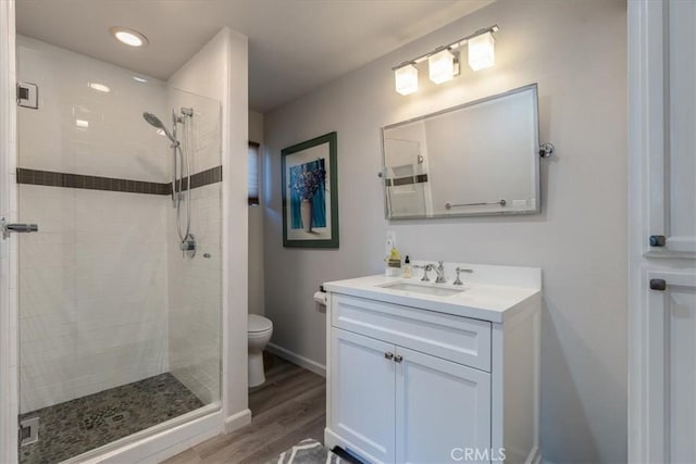 bathroom featuring hardwood / wood-style flooring, vanity, toilet, and a tile shower