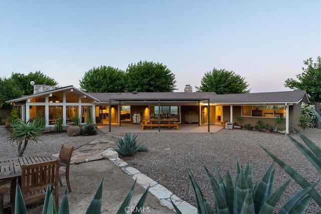 back house at dusk featuring a patio