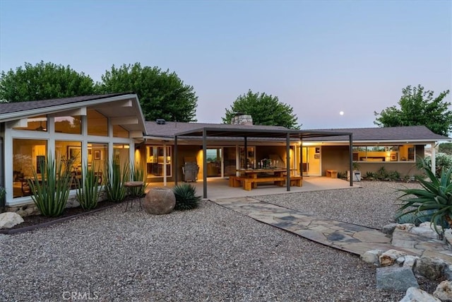 back house at dusk featuring a patio