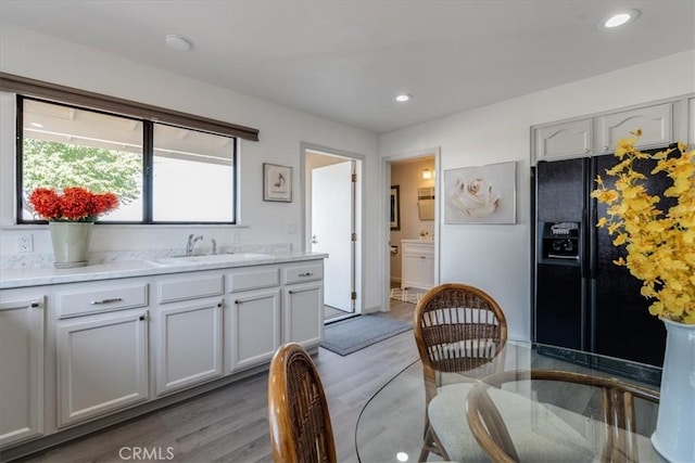 kitchen with sink, black refrigerator with ice dispenser, hardwood / wood-style floors, and white cabinets