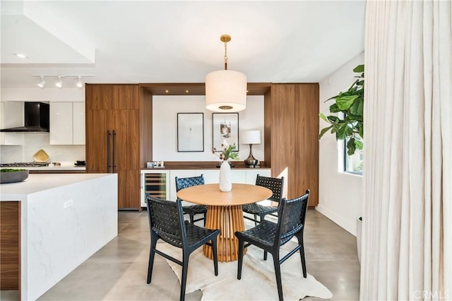 dining space with rail lighting, wine cooler, and finished concrete floors