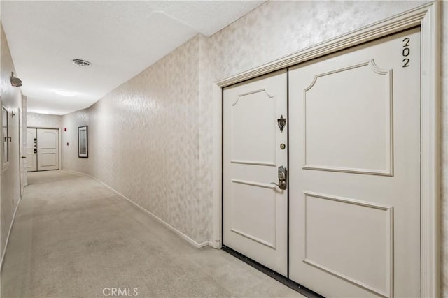 hall featuring baseboards, visible vents, light colored carpet, and wallpapered walls