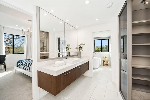 ensuite bathroom with vanity, a wealth of natural light, a soaking tub, and a chandelier