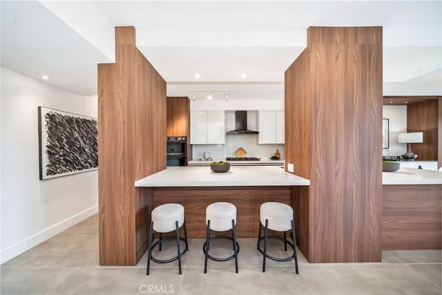 kitchen featuring modern cabinets, wall chimney range hood, a kitchen bar, and white cabinets