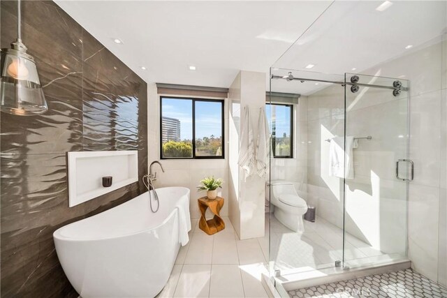 bathroom featuring toilet, plus walk in shower, tile patterned flooring, and tile walls