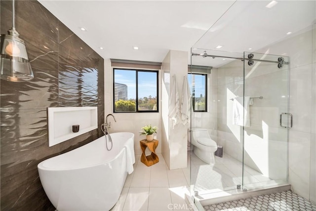 bathroom featuring a stall shower, a freestanding tub, tile walls, toilet, and tile patterned flooring