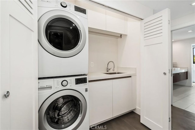 washroom featuring dark tile patterned flooring, a sink, stacked washer / dryer, and laundry area